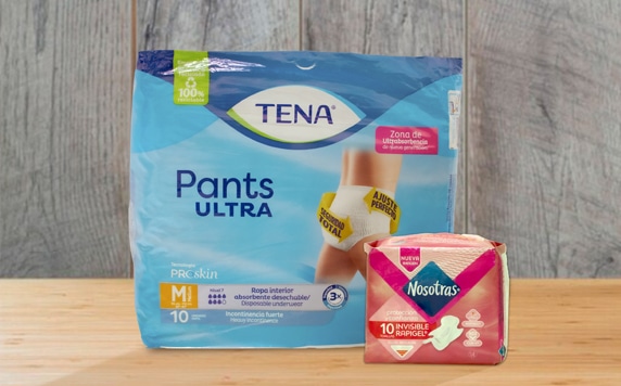 La imagen muestra dos paquetes de productos para la incontinencia. A la izquierda, un paquete de TENA Pants Ultra, talla M, que contiene 10 unidades de ropa interior absorbente desechable para incontinencia fuerte. El paquete destaca la zona de ultraabsorbencia y el ajuste perfecto. A la derecha, un paquete de Nosotras Invisible Rapigel, con 10 unidades de protectores diarios. Ambas cajas están sobre una superficie de madera. La imagen parece ser una publicidad o presentación de productos para el cuidado personal dirigidos a adultos con problemas de incontinencia. Los colores predominantes son el azul claro (TENA) y el rosa (Nosotras), dando una sensación de limpieza y discreción, características importantes para este tipo de productos.